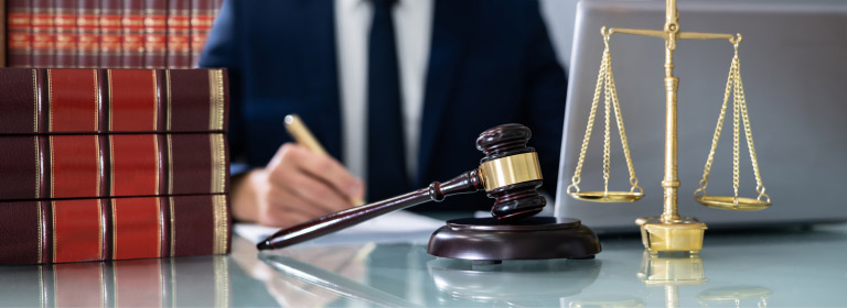 lawyer behind a desk with books, a gavel, and a scale of justice